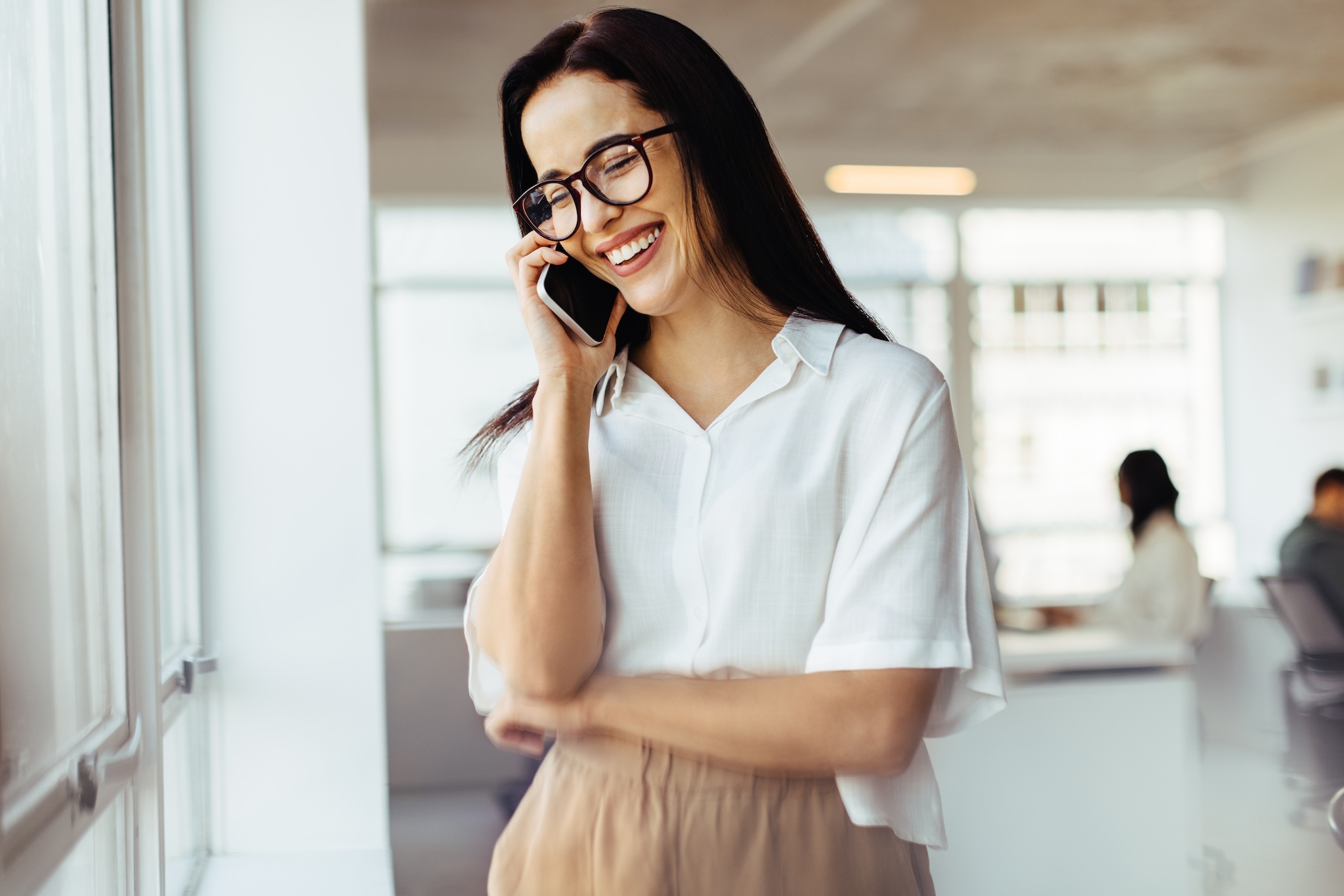Happy business woman having a phone call while standing in an office. Female business executive talking to clients on the phone.